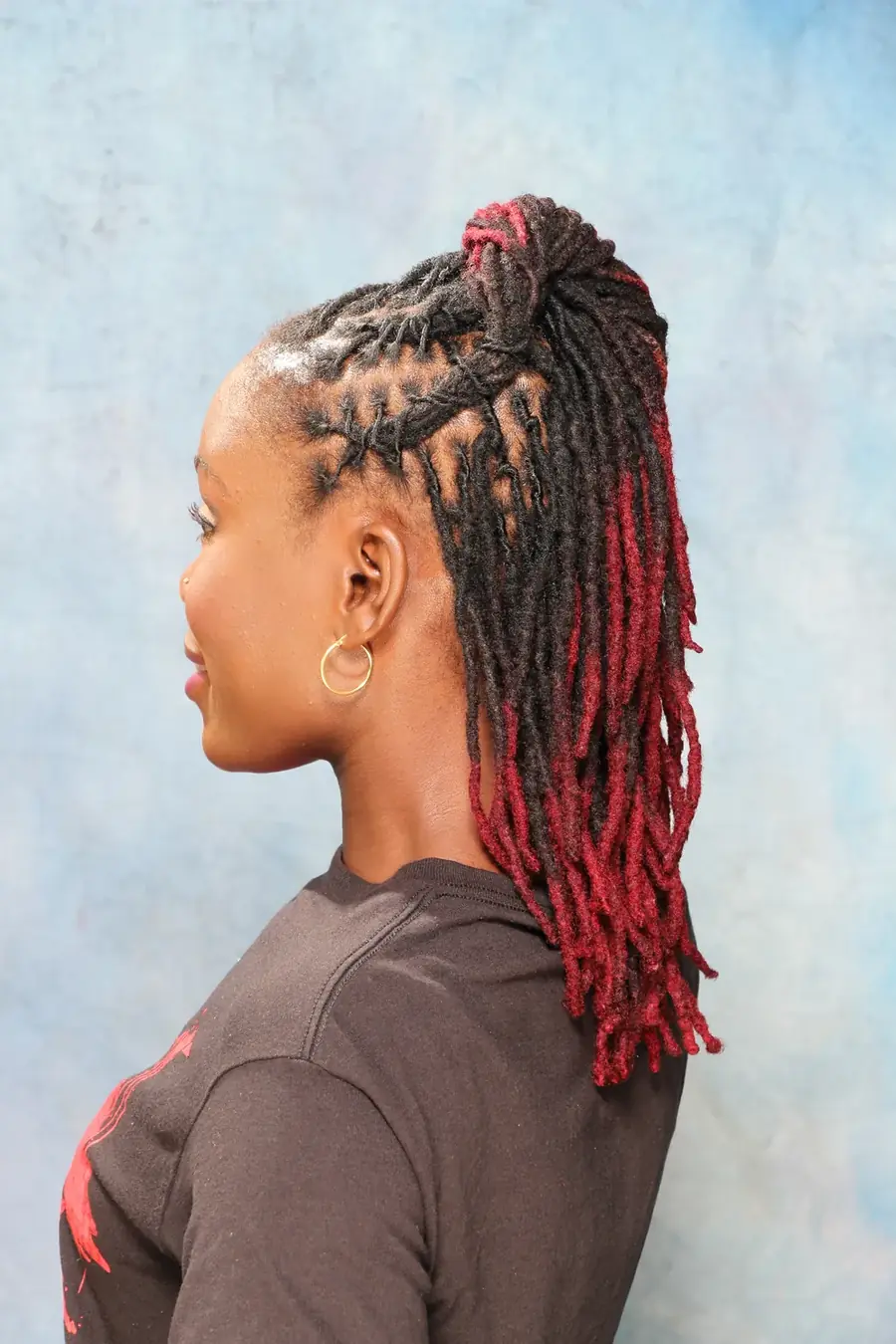 Side view of a client wearing red-tipped Sisterlocks pulled into a high ponytail